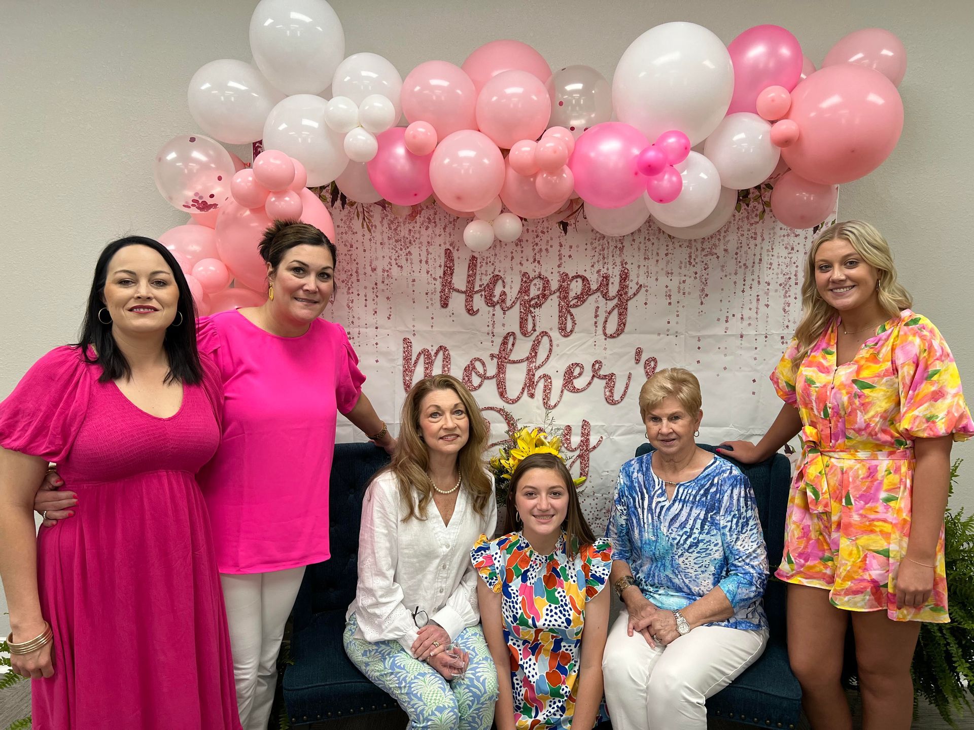 Group of women posing in front of a Mother's Day backdrop with balloons.