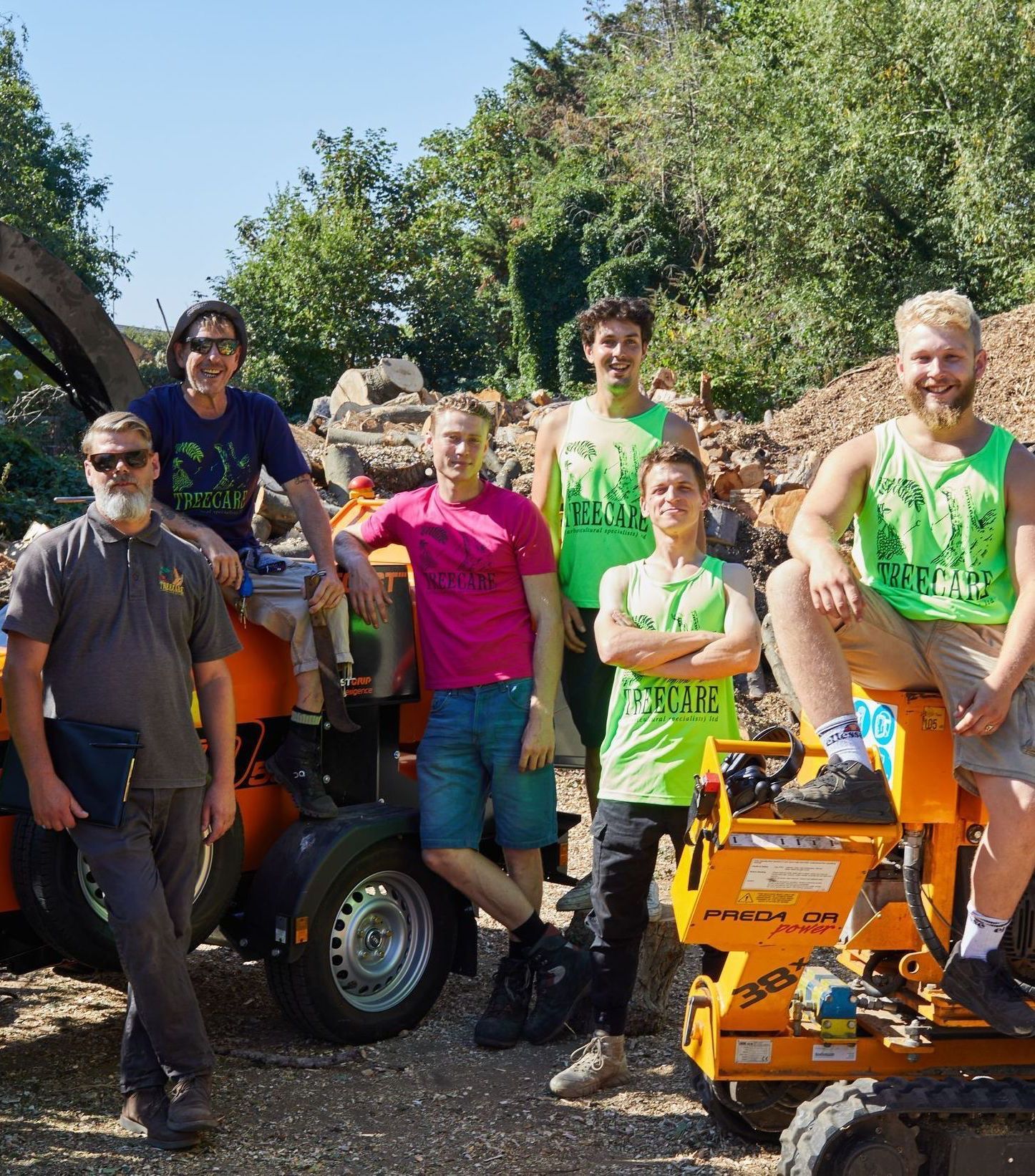 Group of people posing with machinery outdoors. Some wear neon green shirts, others casual attire.