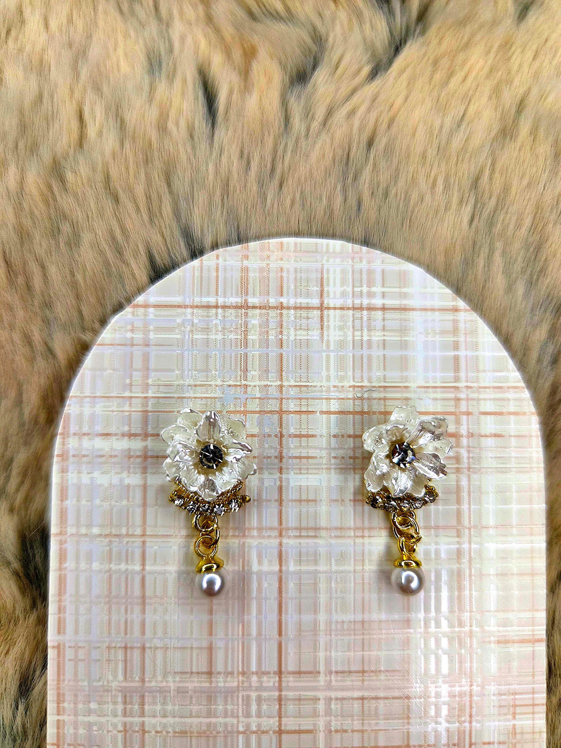 Een paar kleine oorbellen met gouden en parelhangers op een beige geruite achtergrond.