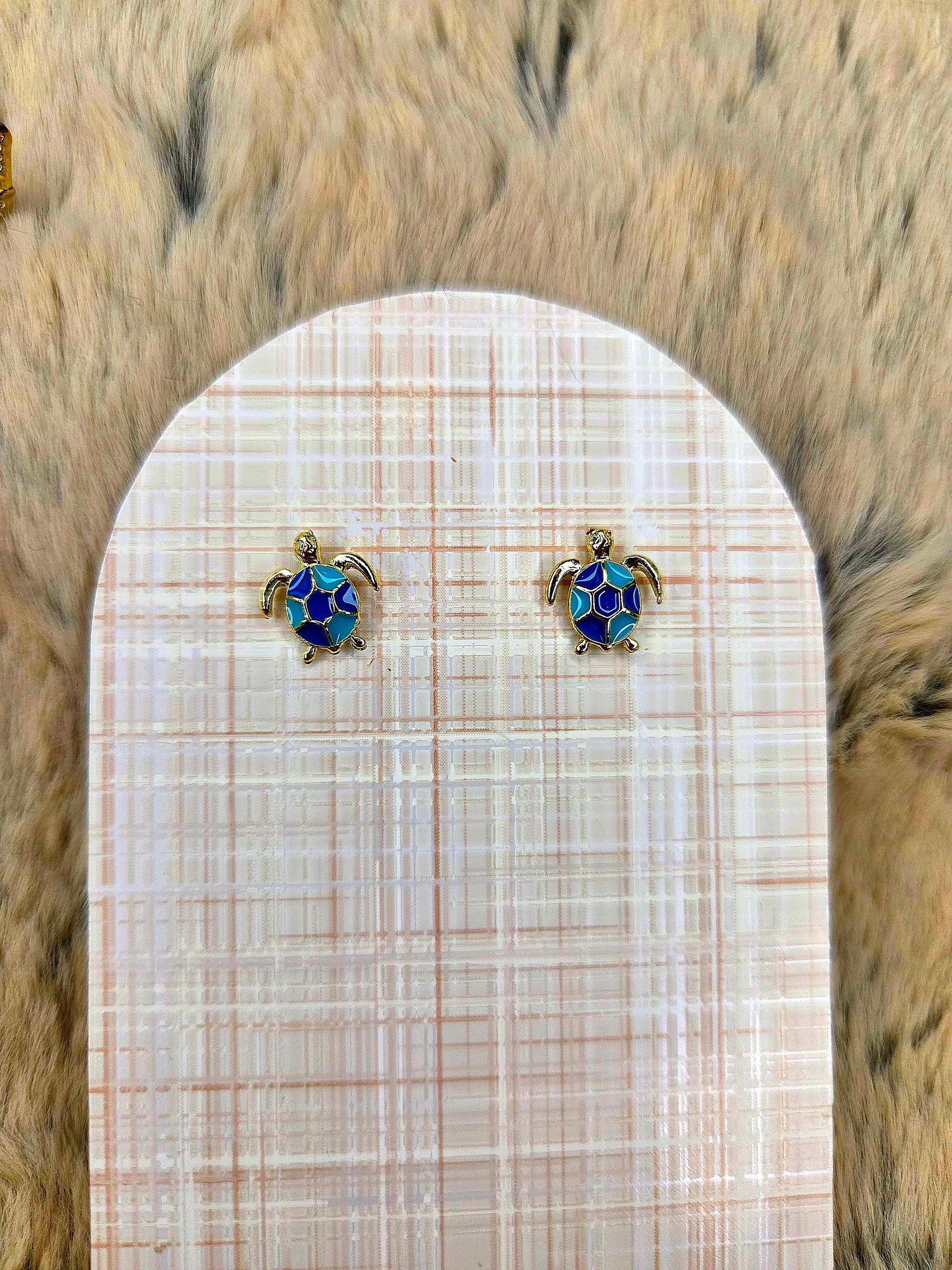 Twee kleine blauw-gouden oorknopjes op een wit kaartje tegen een houten achtergrond.