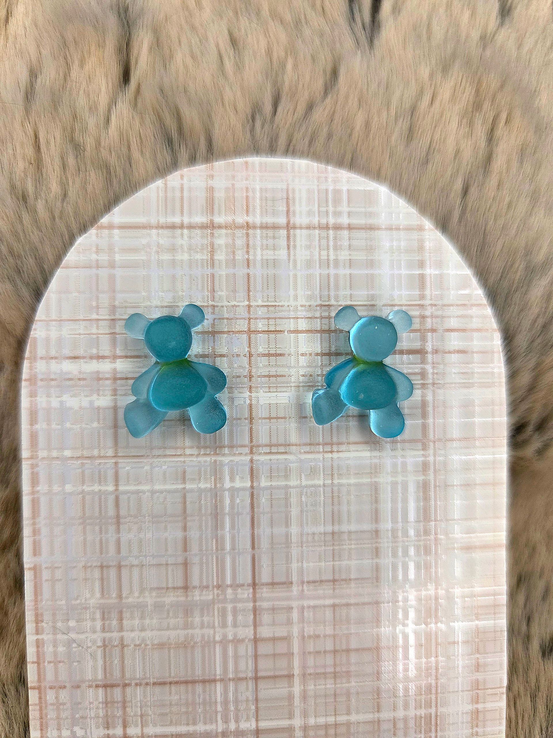 Turquoise oorknopjes met teddybeermotief op een wit, gestructureerd kaartje.