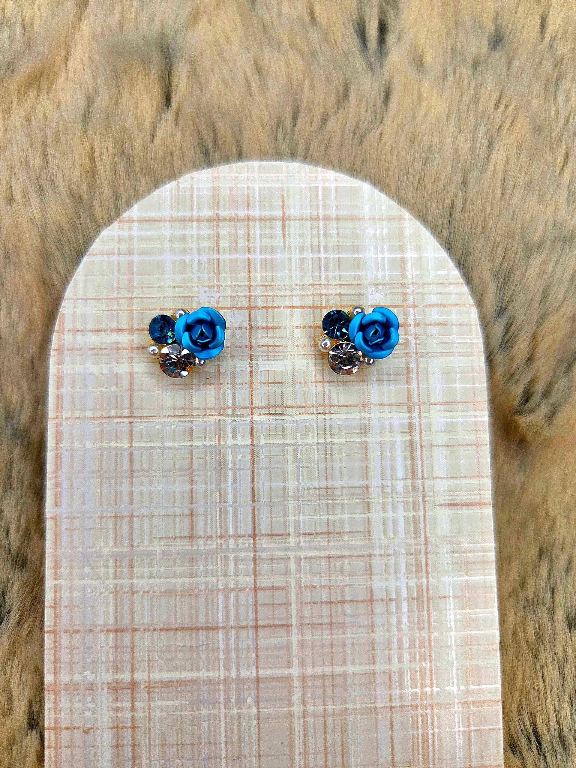 Een paar kleine blauwe oorknopjes met edelstenen op een beige, gestructureerd presentatiekaartje.