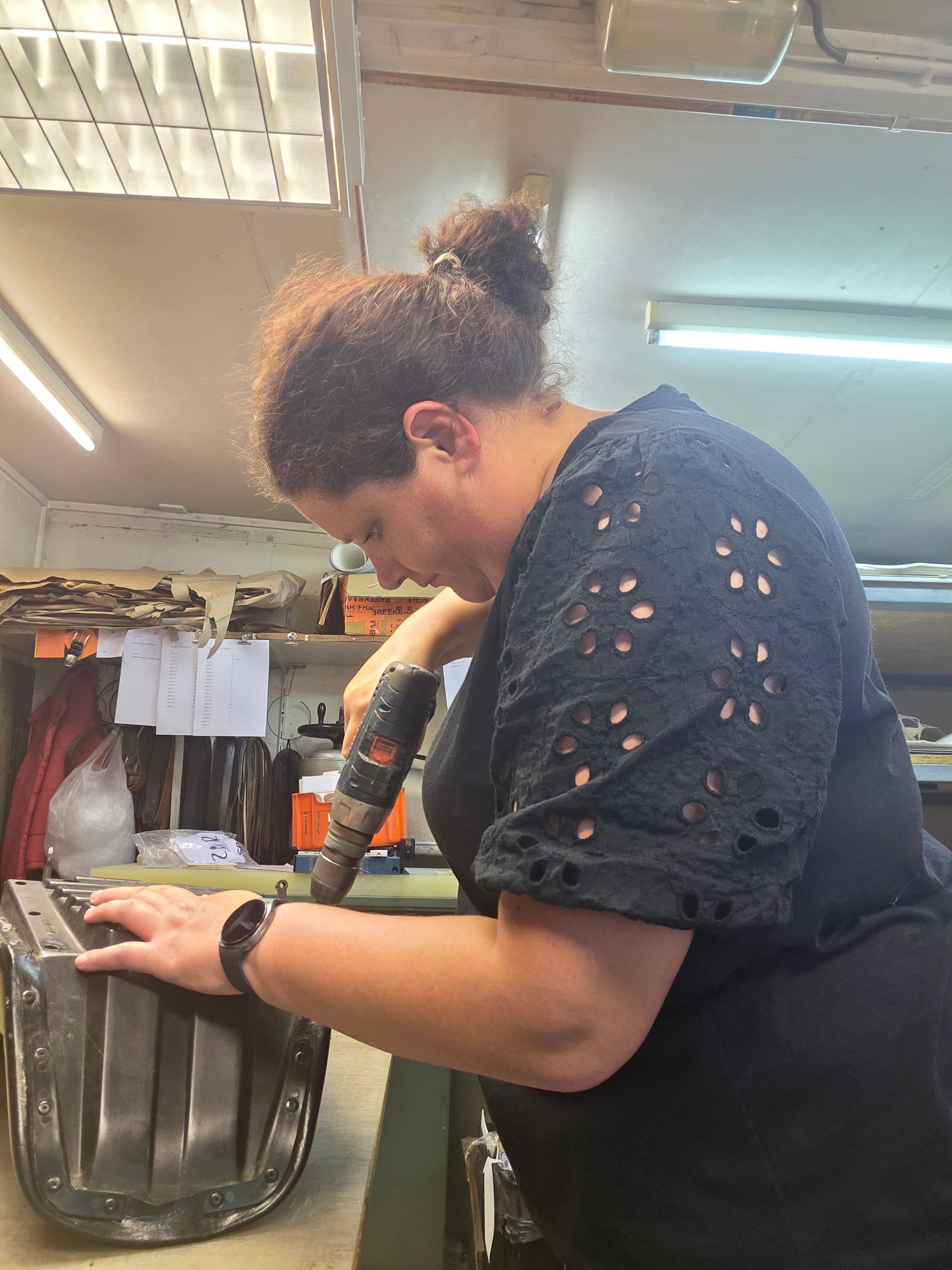 Een persoon die met zijn handen aan een metalen voorwerp werkt in een werkplaats, onder fel TL-licht.