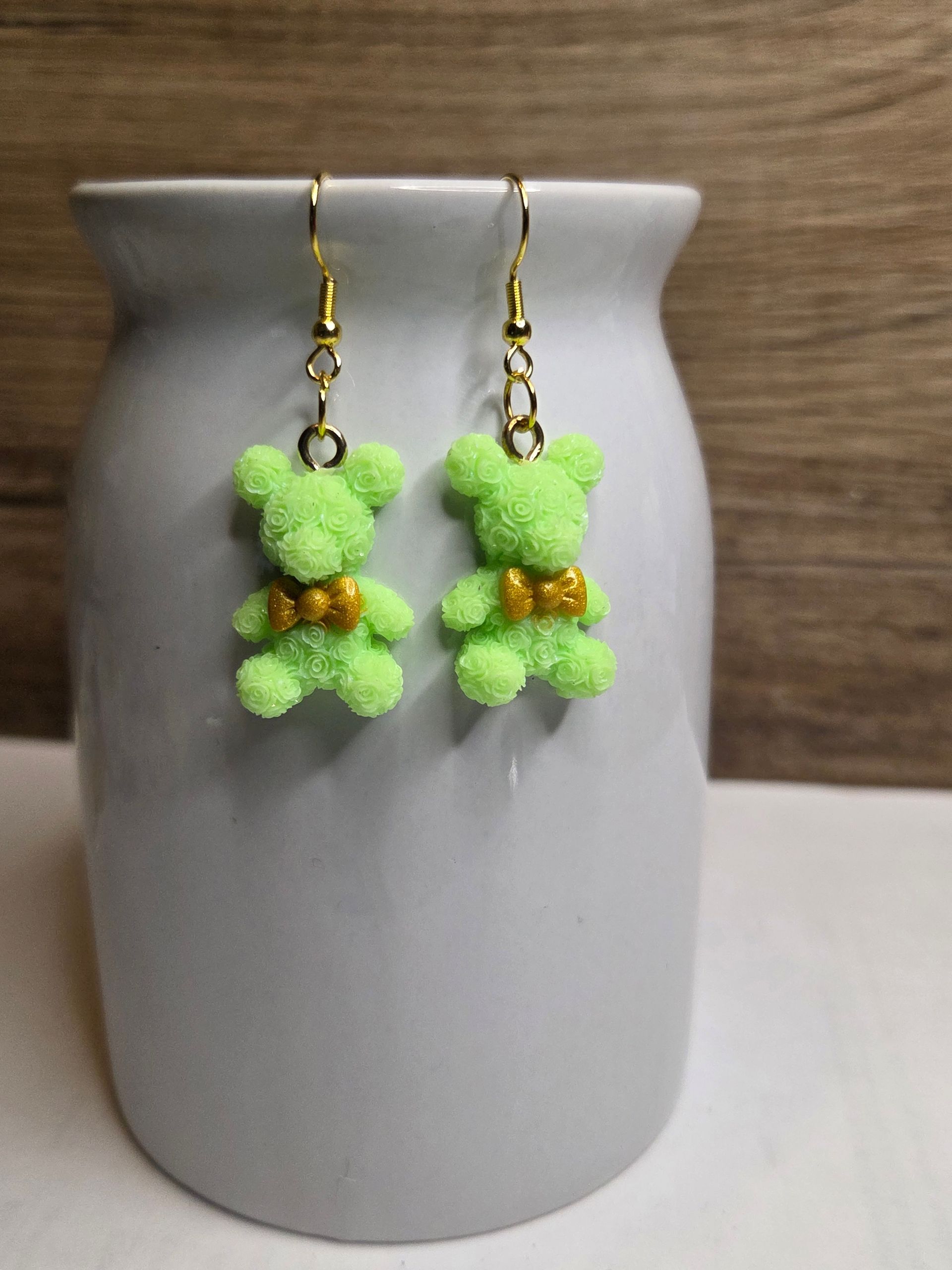 Lichtgroene teddybeer-oorbellen met gouden strikjes, hangend aan gouden oorhaakjes.