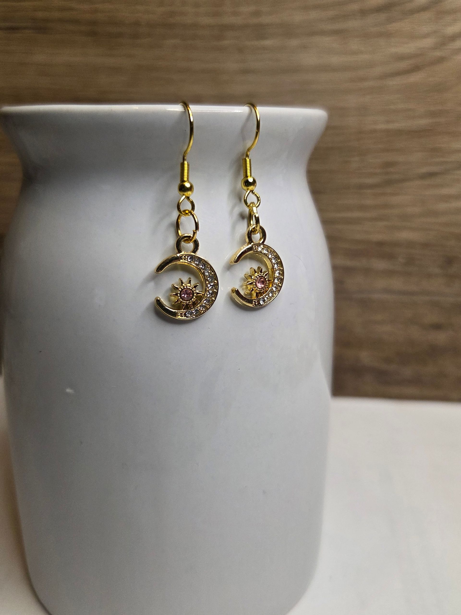 Gouden oorbellen in de vorm van een halve maan met strass-steentjes, hangend aan een witte vaas.