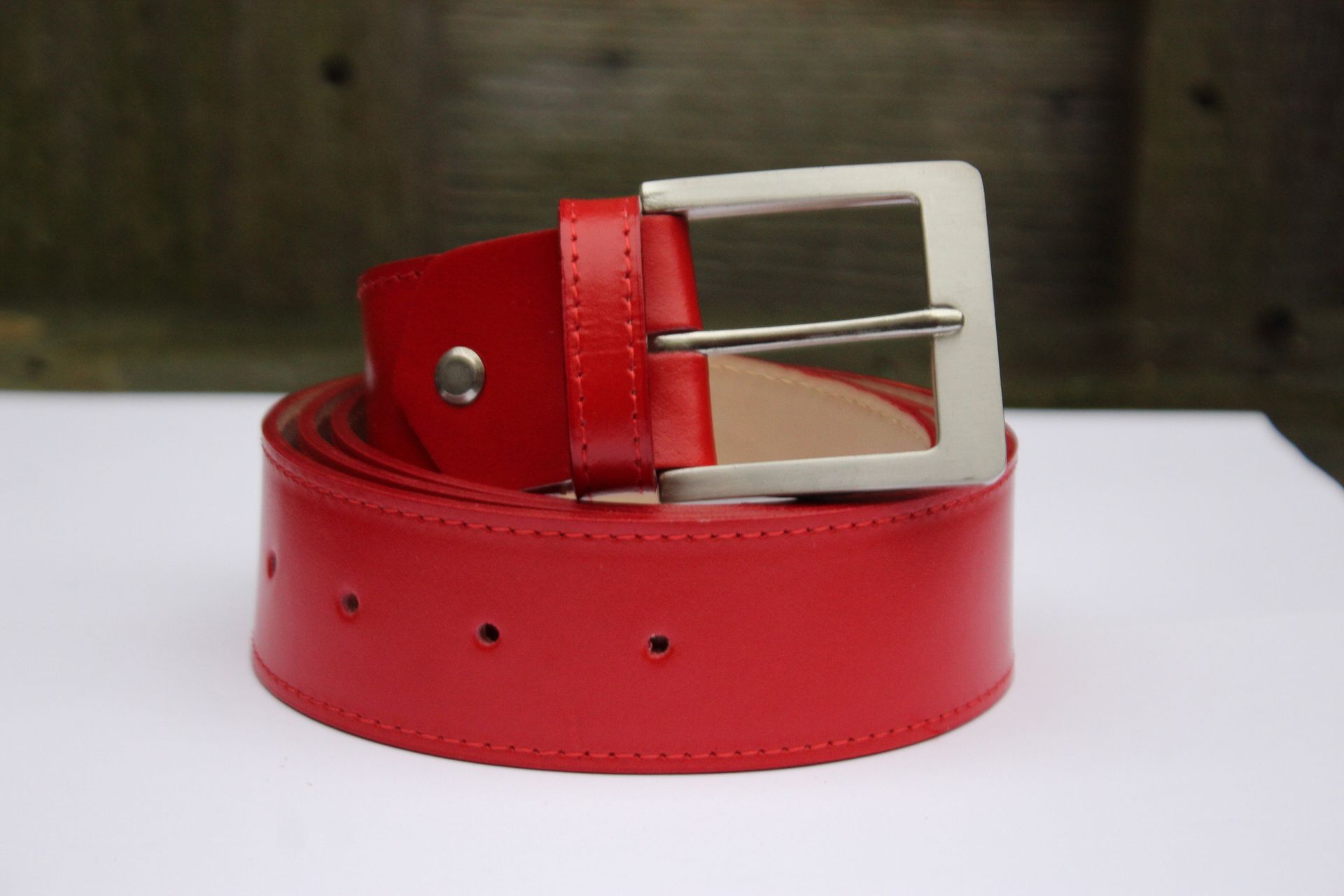 Rode leren riem met een zilveren gesp, opgerold op een witte ondergrond.