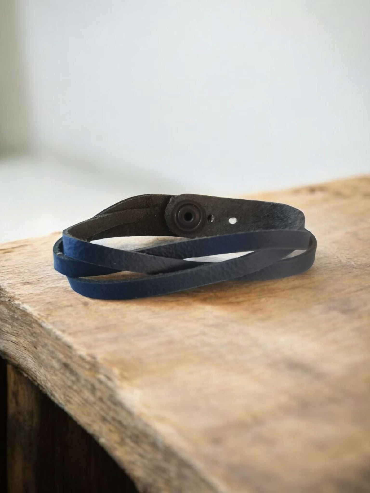 Blauwe leren wikkelarmband op een houten ondergrond, met een ronde sluiting.