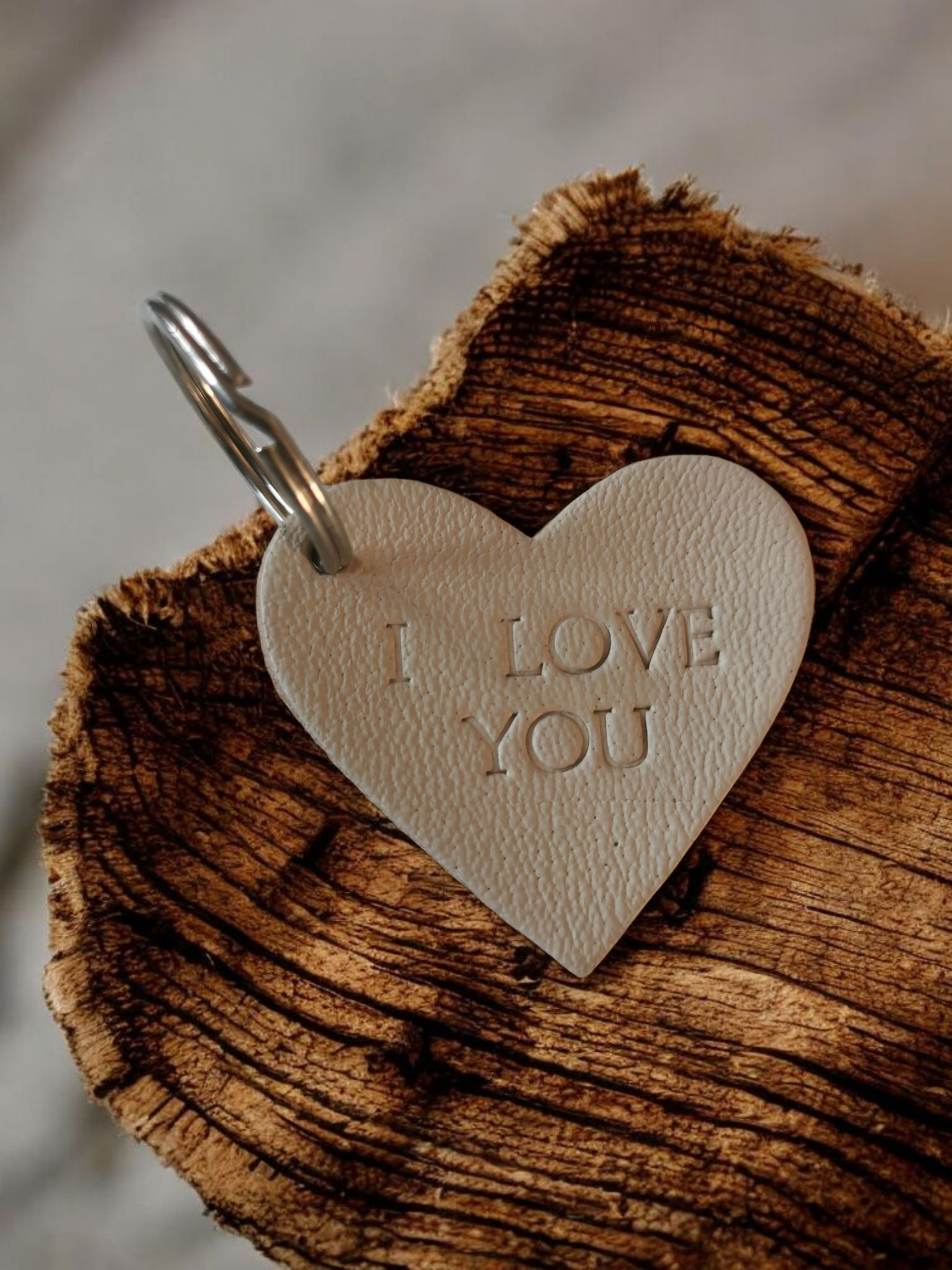Hartvormige leren sleutel hanger met de tekst "I love you" in reliëf, rustend op een ruw houten oppervlak.