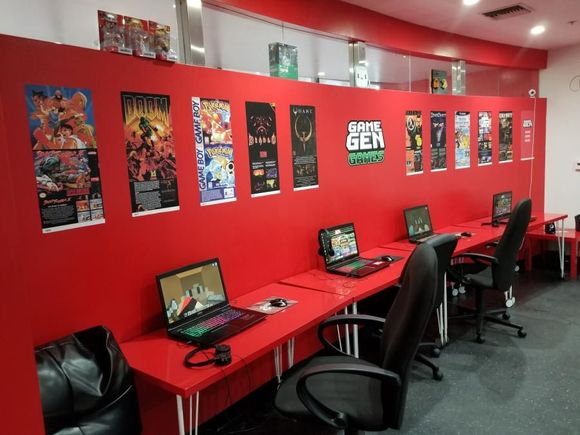 Red-walled gaming area with laptops, posters, and black chairs.