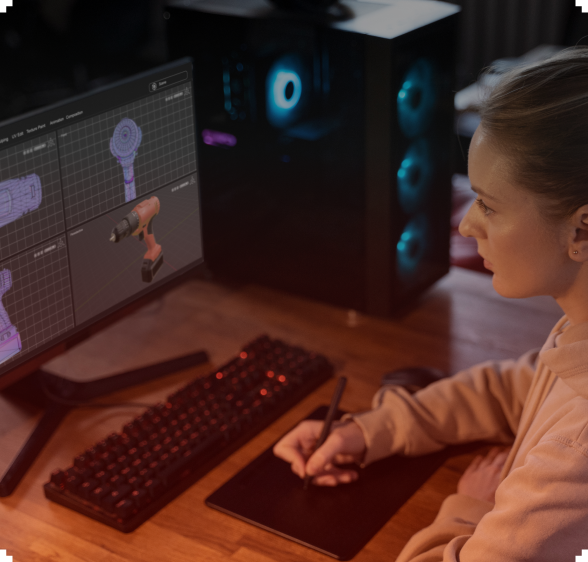 Woman using a graphics tablet and computer with 3D modeling software at a desk, near a lit computer tower.