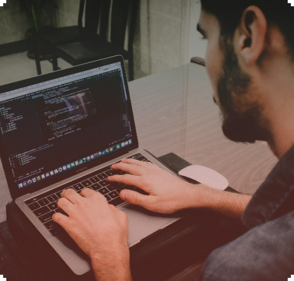 Man coding on a laptop, hands typing on the keyboard, indoor setting.