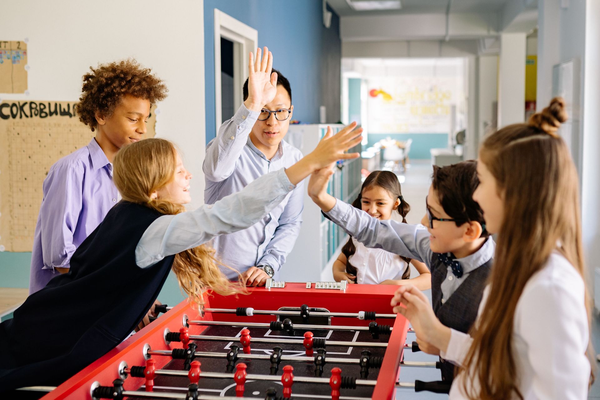 People high-five around a red foosball table in a bright indoor play area