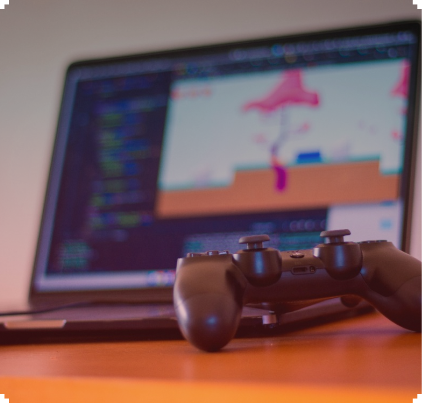 Laptop displaying a video game, with a gamepad resting in front of it on a desk.