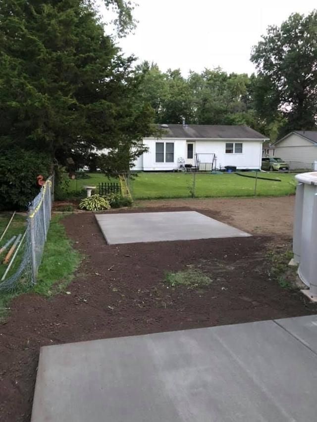 A concrete slab in a backyard with a house, chain-link fence, and trees.