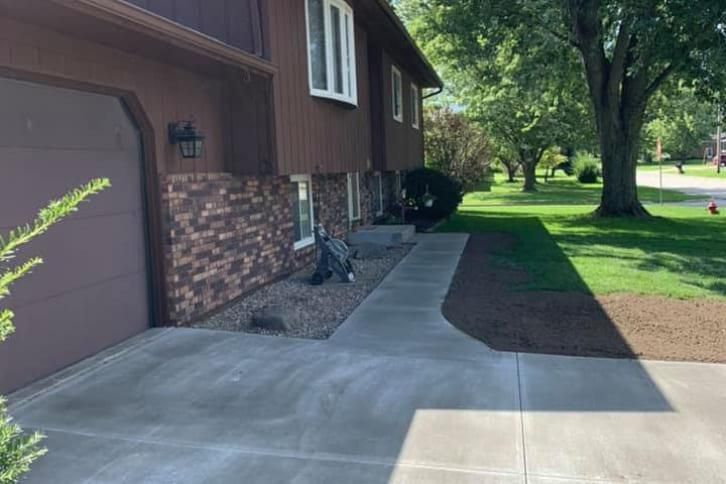 Brown house with brick facade, concrete walkway, green lawn, sunny day.