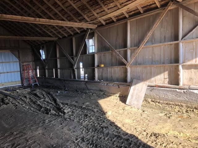 Interior of an old barn with wooden beams, siding, and dirt floor. A ladder leans against a side entrance.