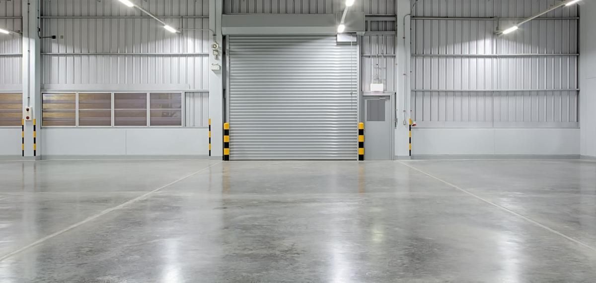 Interior of an empty warehouse with a large closed metal door. Concrete floor. Bright lighting.