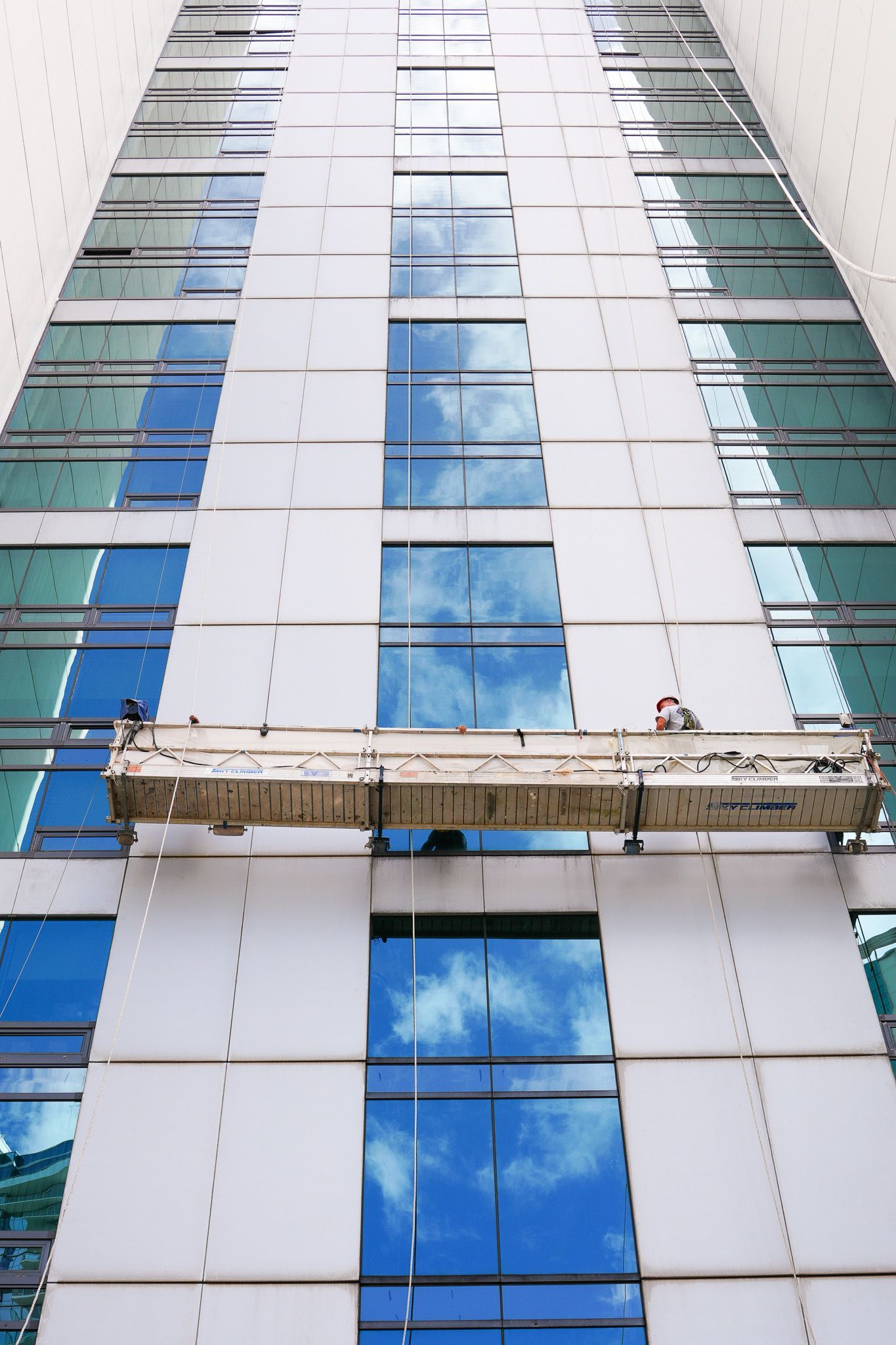Tall modern glass building with a suspended maintenance platform near the lower floors