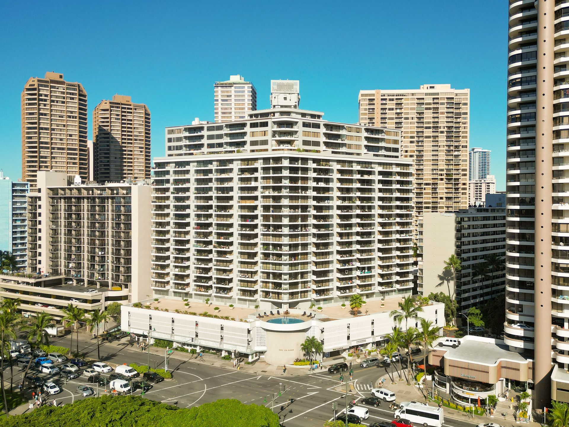 City skyline with a large white hotel, high-rise apartments, and a parking lot in front under a clear blue sky