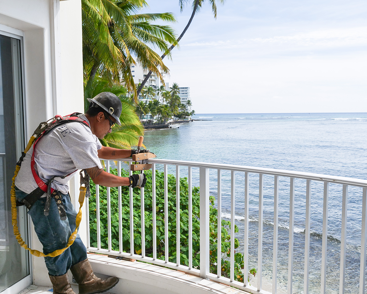 A man is working on a balcony overlooking the ocean.