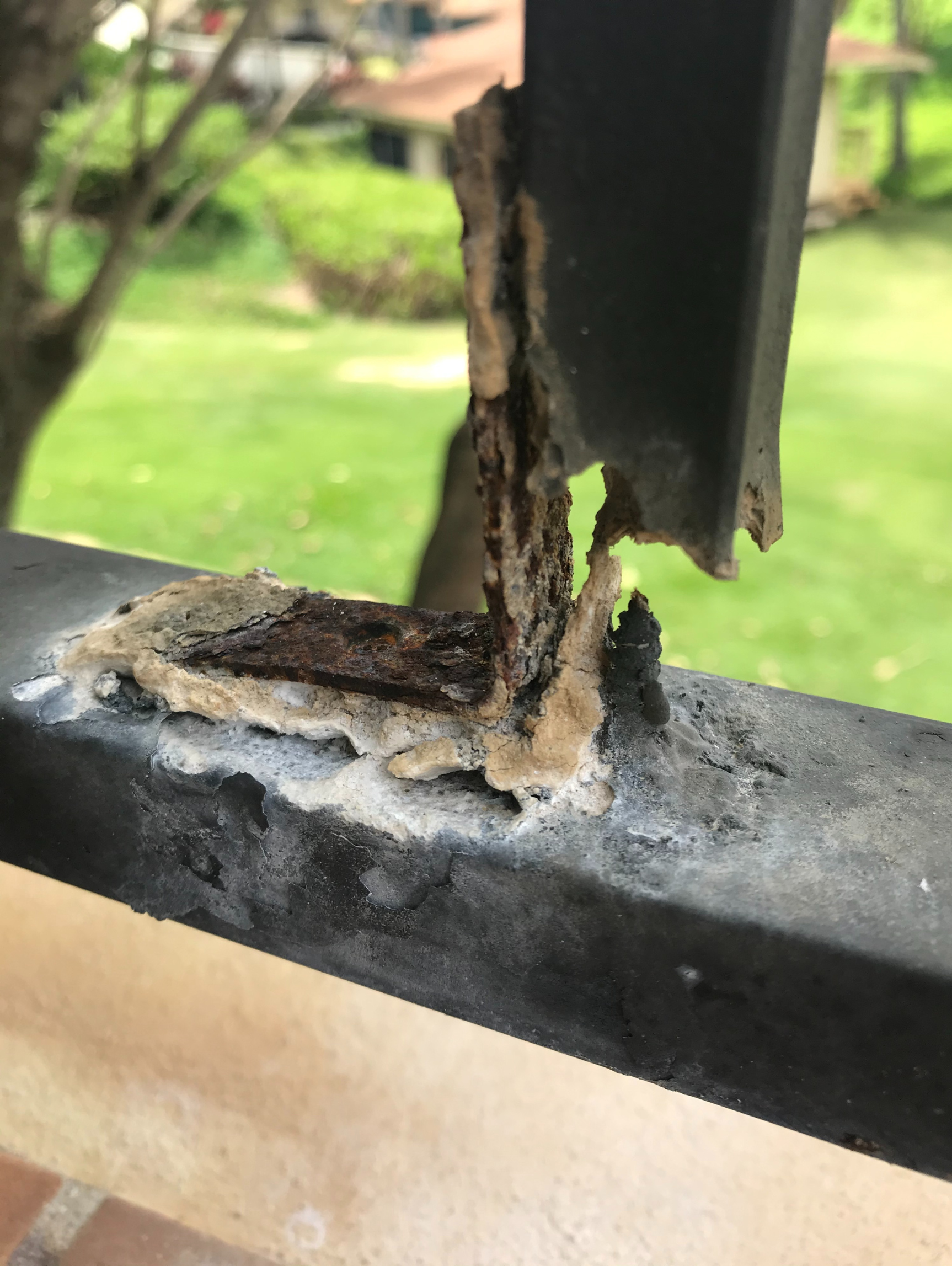 Close-up of a broken black metal post with rust and peeling paint on a ledge outdoors