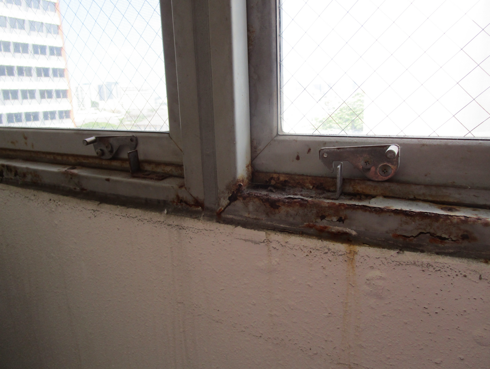 Dirty window sill with rust stains and peeling paint beneath two windows.