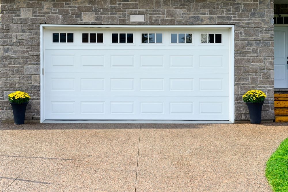 A white garage door is sitting in front of a brick house.
