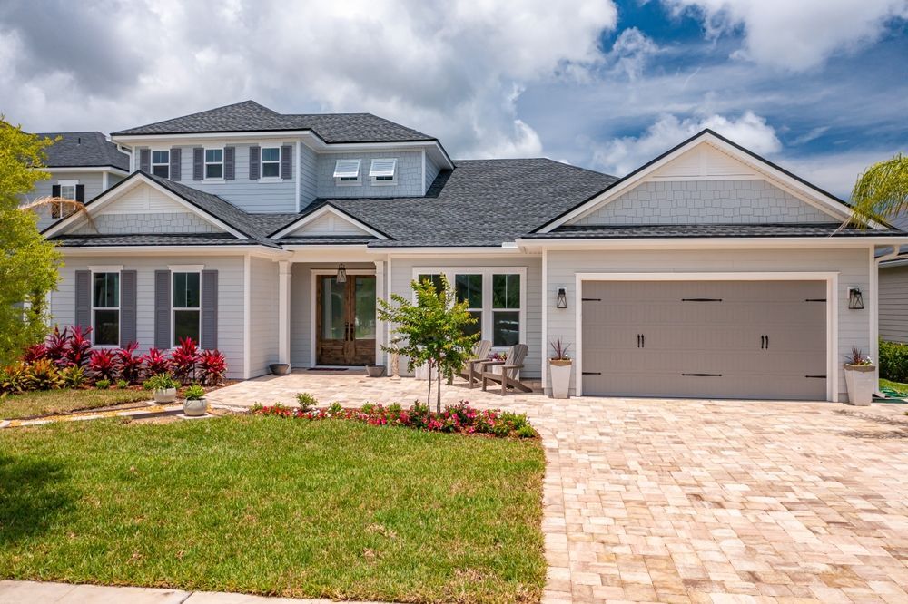 A large white house with a gray garage door and a brick driveway.