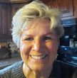 Smiling older woman with short, gray hair in a kitchen, wearing a gray sweater.