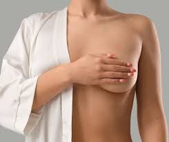 Woman in a white robe, covering one breast with her hand, gray background.