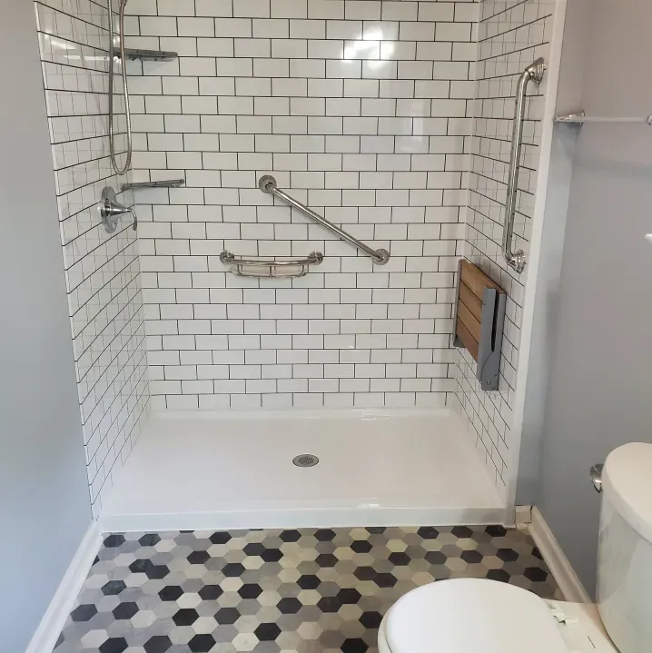 Small bathroom with a white tiled walk-in shower, grab bars, bench, and black-and-white hex floor tiles