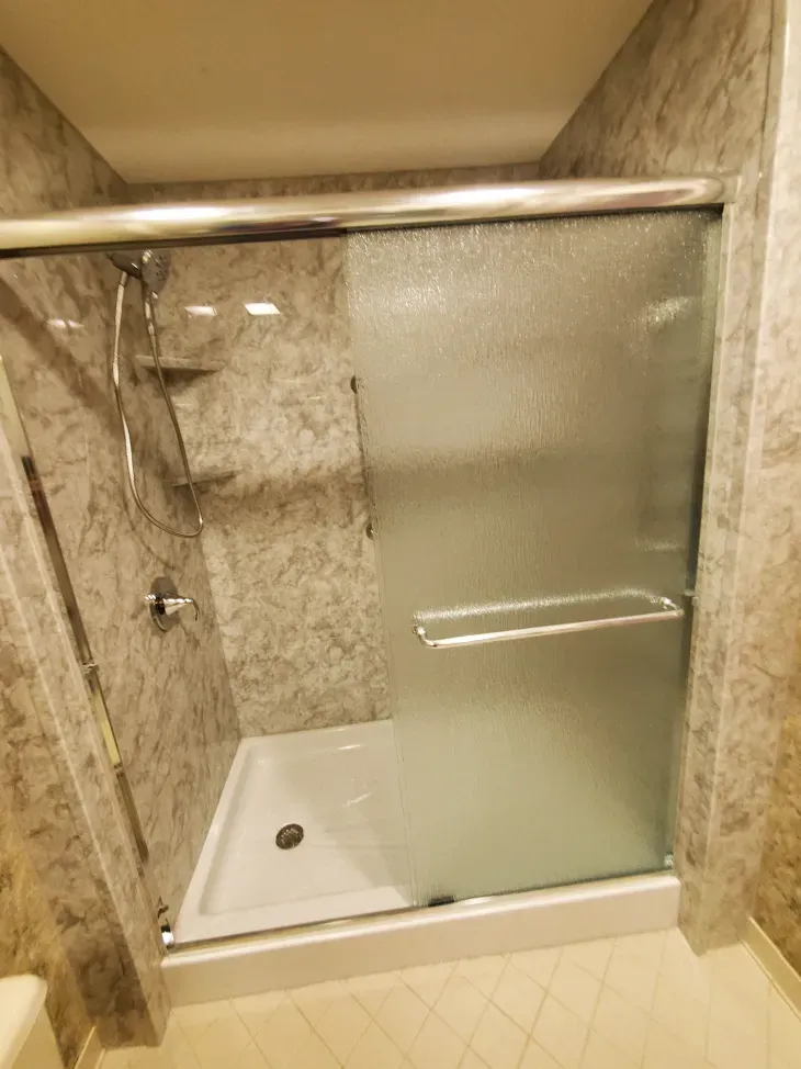 Glass shower stall with marble walls, frosted sliding door, and a white shower pan