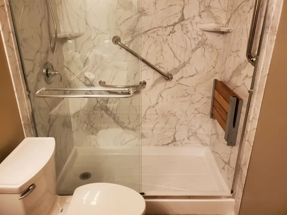 Accessible bathroom shower with grab bars, a fold-down seat, and marble-patterned tile.