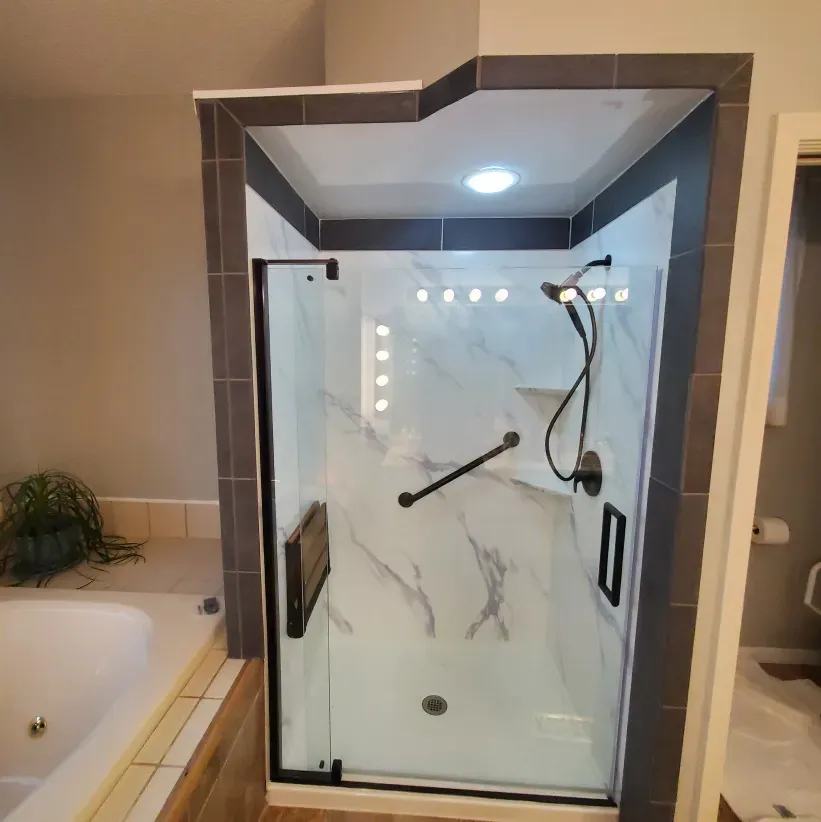 Modern glass shower stall with marble-look tile, chrome fixtures, and a built-in light above the door.