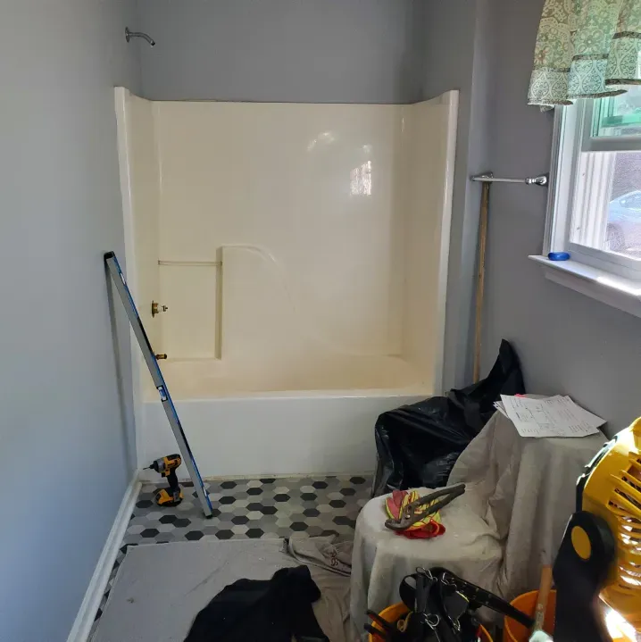 Bathroom with tub and cream shower surround, gray walls, patterned floor, and tools/ladder indicating renovation