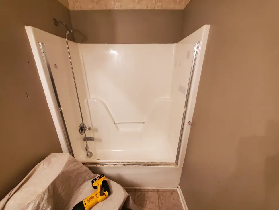 Corner shower stall with white door panels, unfinished bathroom walls, and a yellow tool on the floor