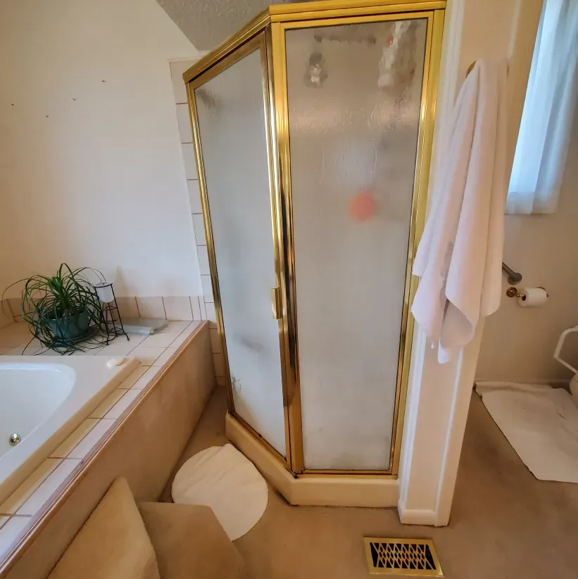 Bathroom with corner glass shower, bathtub, towel, sink, and beige tile floor.