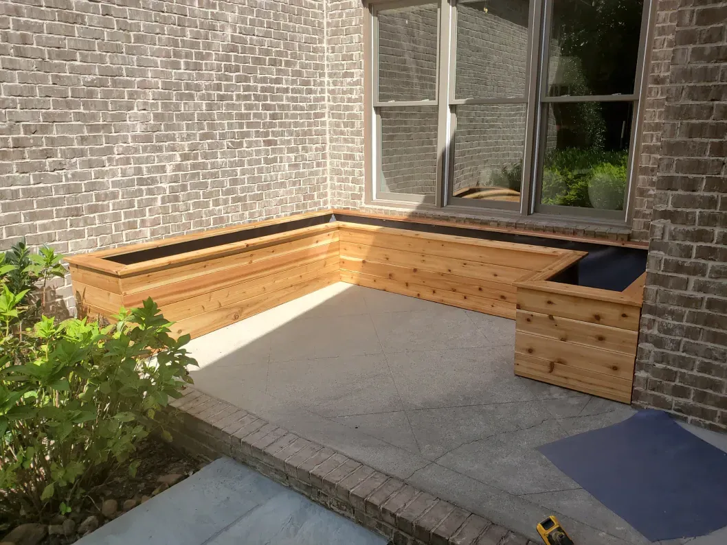 Brick patio corner with built-in wooden bench planters beside a house window