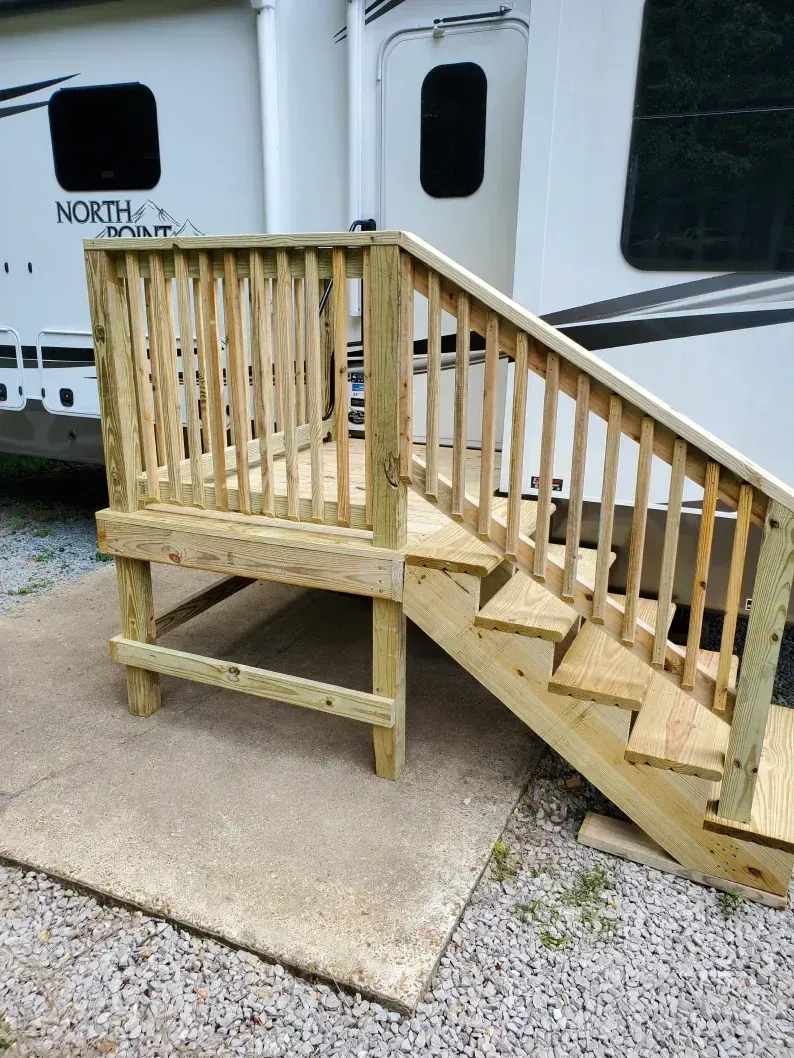 Wooden accessibility ramp with steps leading to a trailer door on gravel and concrete.
