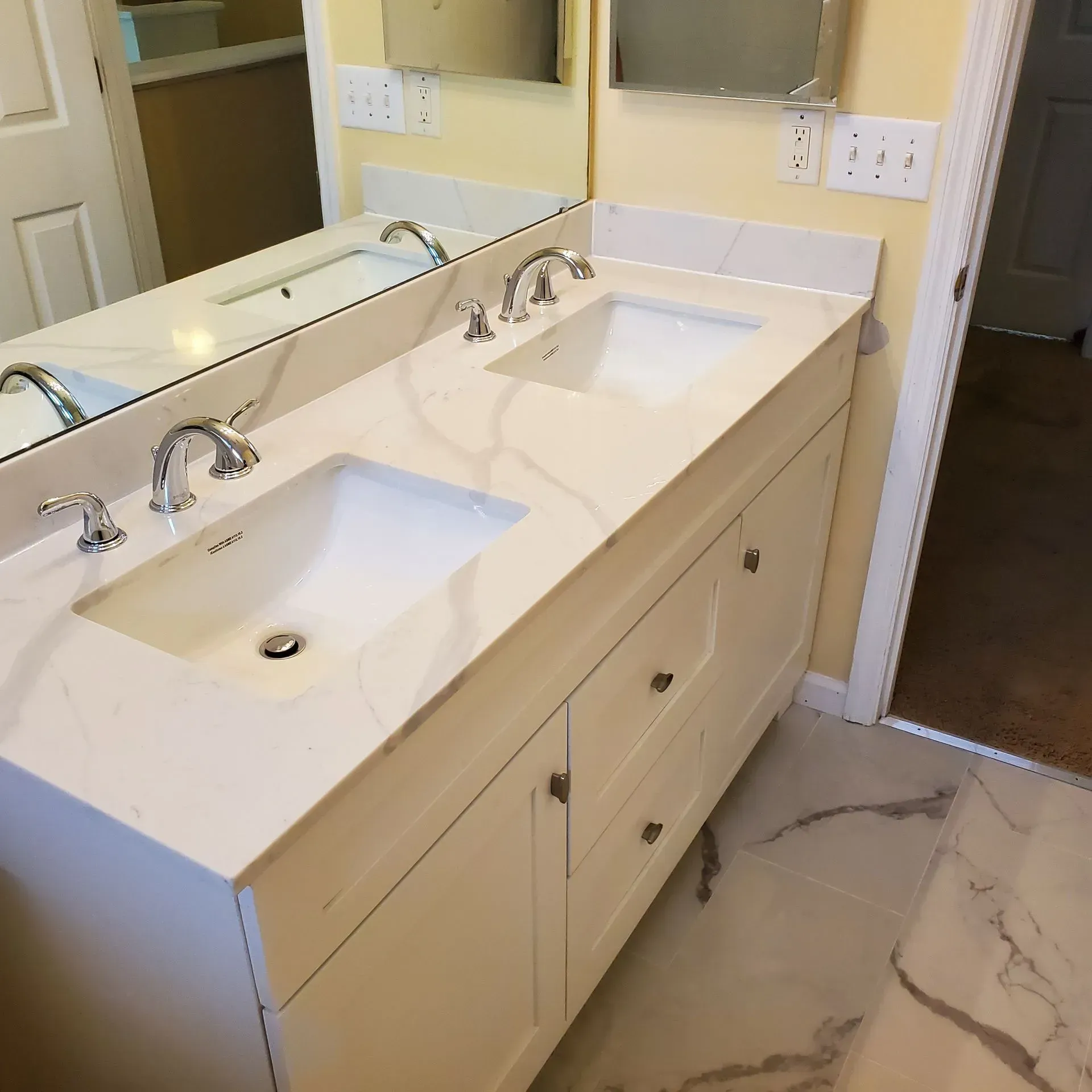 Double bathroom vanity with white sinks, chrome faucets, large mirror, and marble-look tile floor.