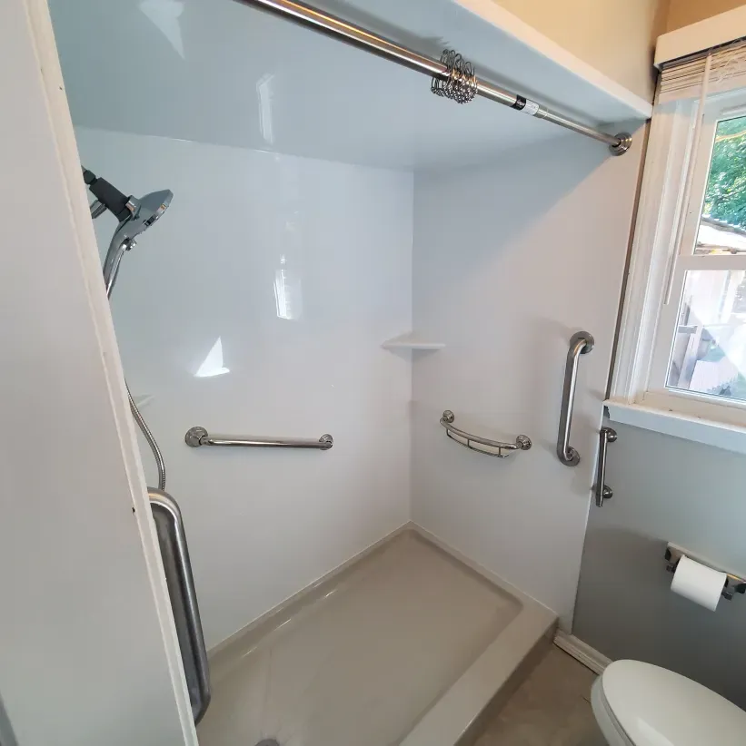 Accessible bathroom with walk-in shower, grab bars, bench, and toilet next to a window