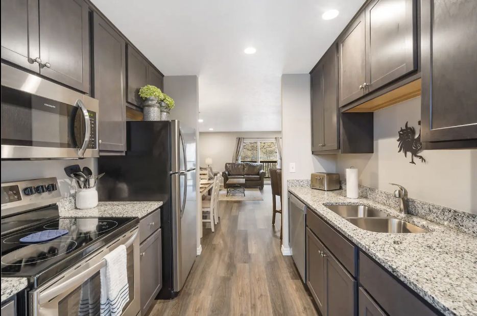 Modern galley kitchen with dark cabinets, granite counters, stainless appliances, and wood-look flooring