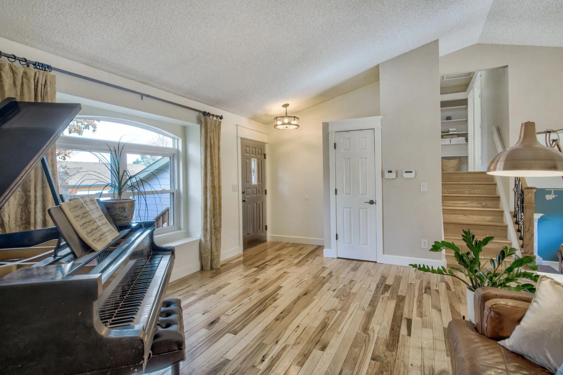 Bright living room with grand piano, hardwood floors, large window, and potted plant