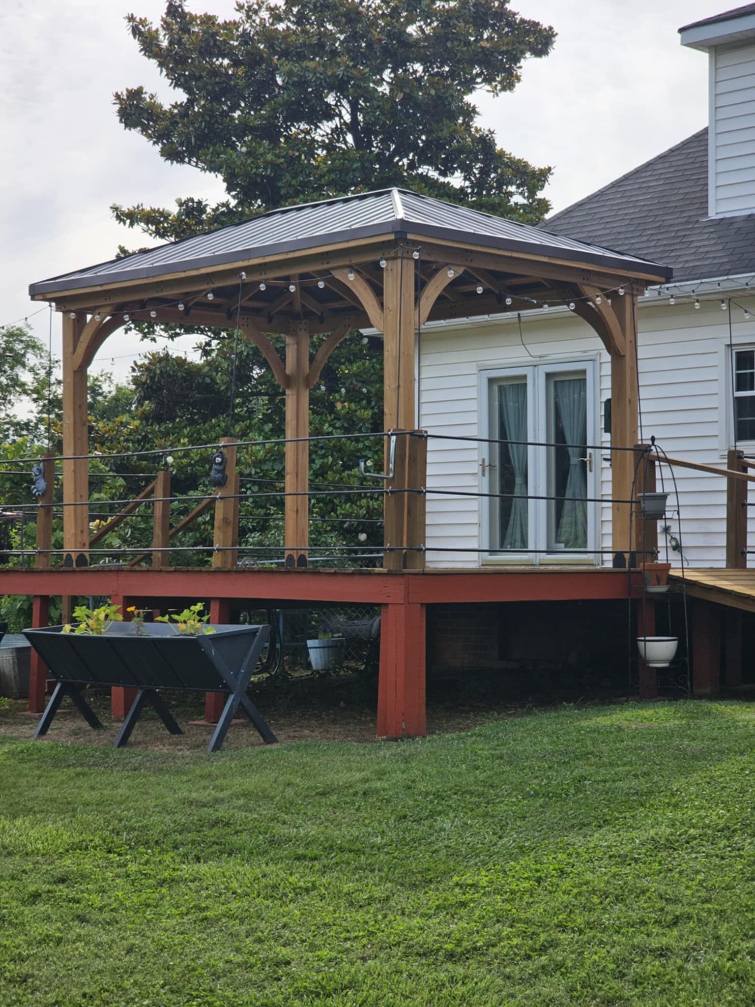 Wooden backyard deck with gazebo, railing, and outdoor seating beside a house