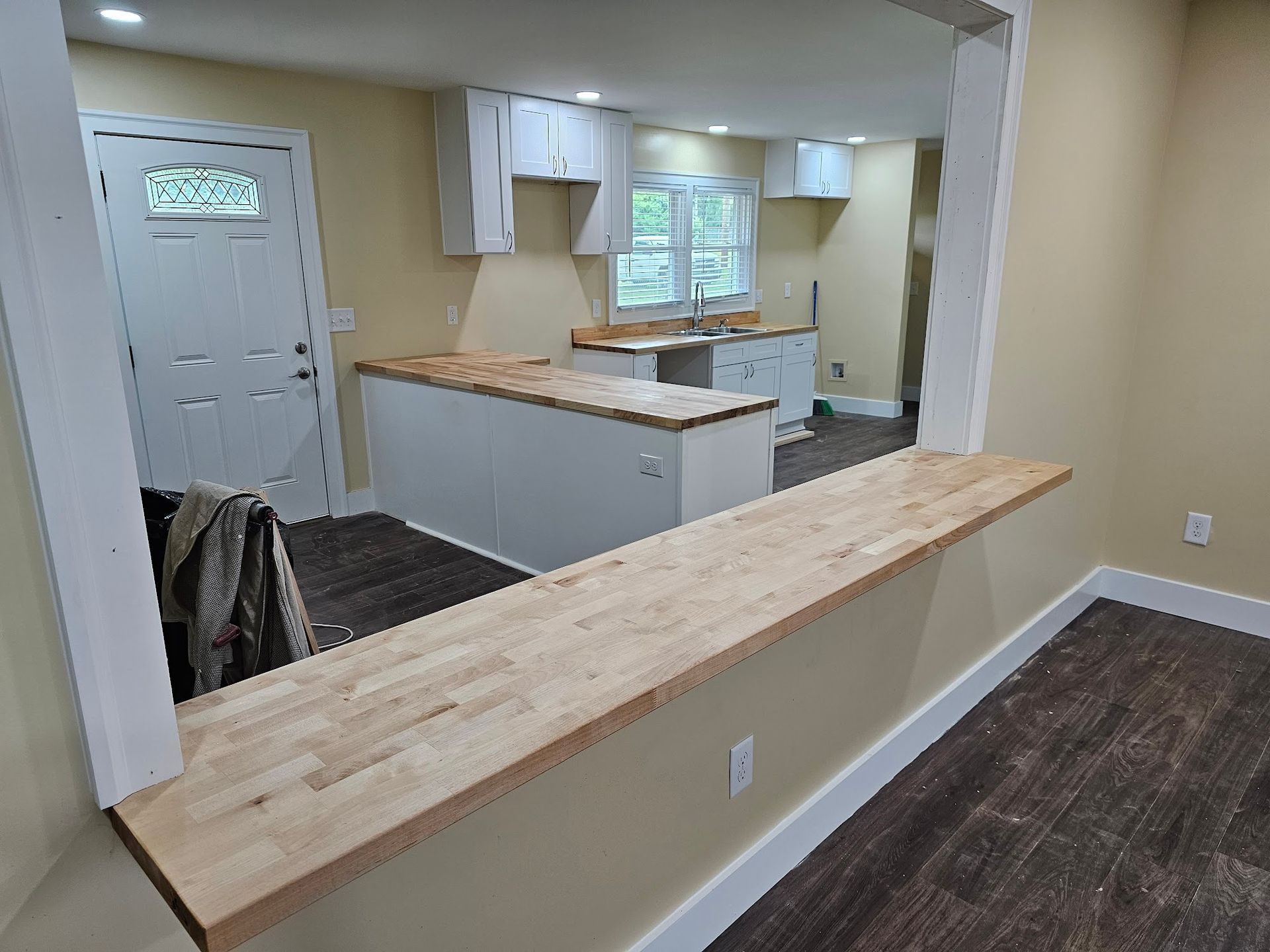 Empty kitchen with white cabinets, wood countertops, and a pass-through opening to the dining area.