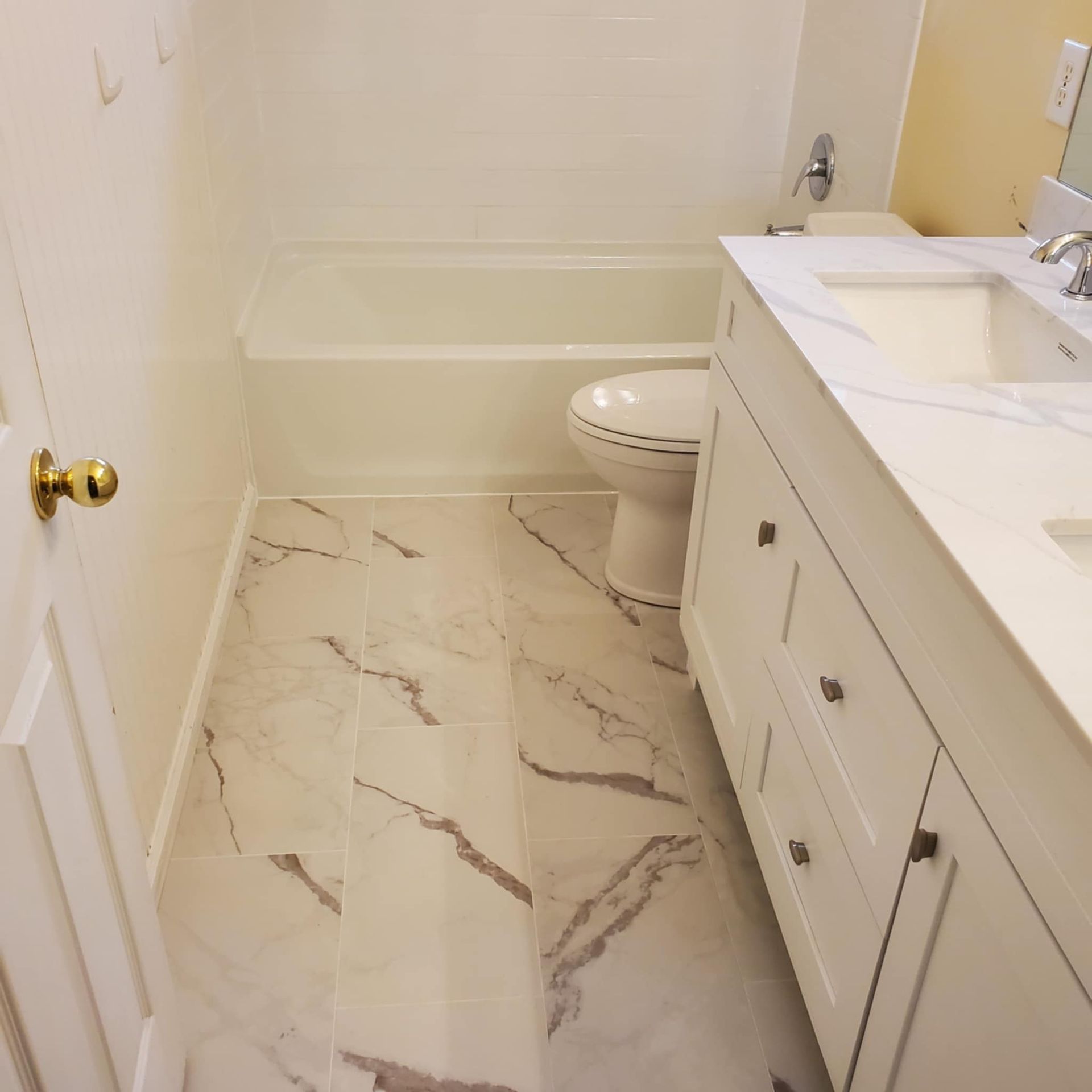 Modern bathroom with marble floor, white vanity, sink, toilet, and bathtub