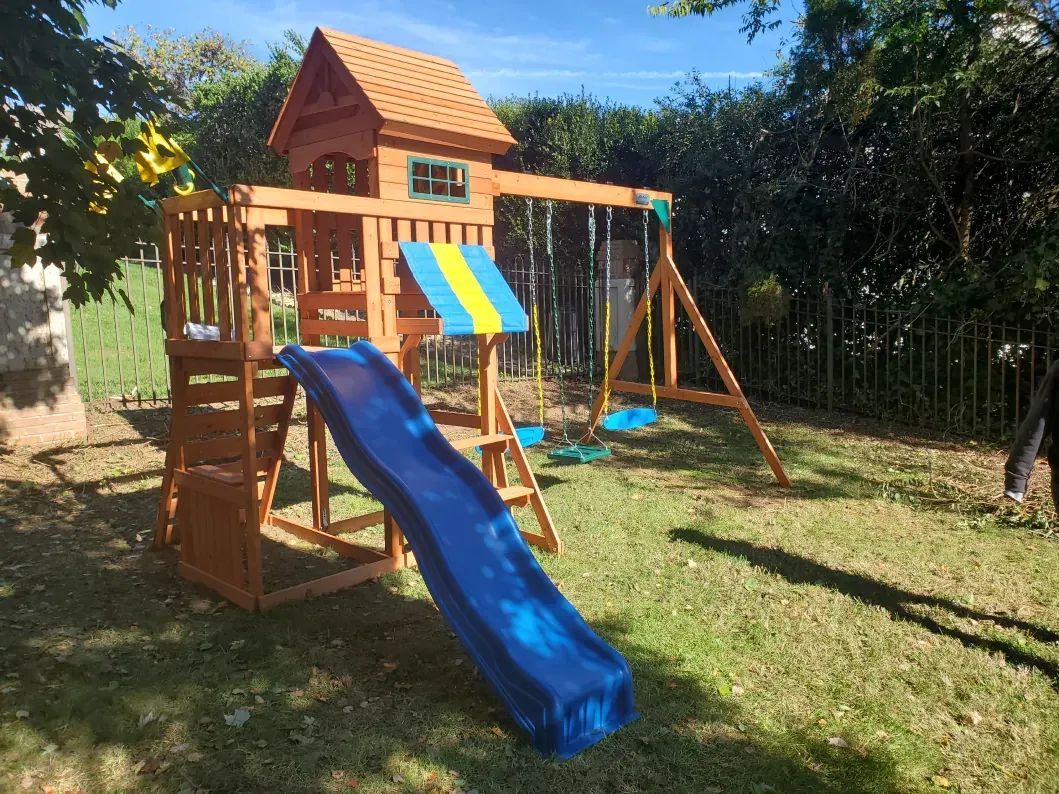 Wooden backyard playset with blue slide, swing, and colorful roof in a sunny yard