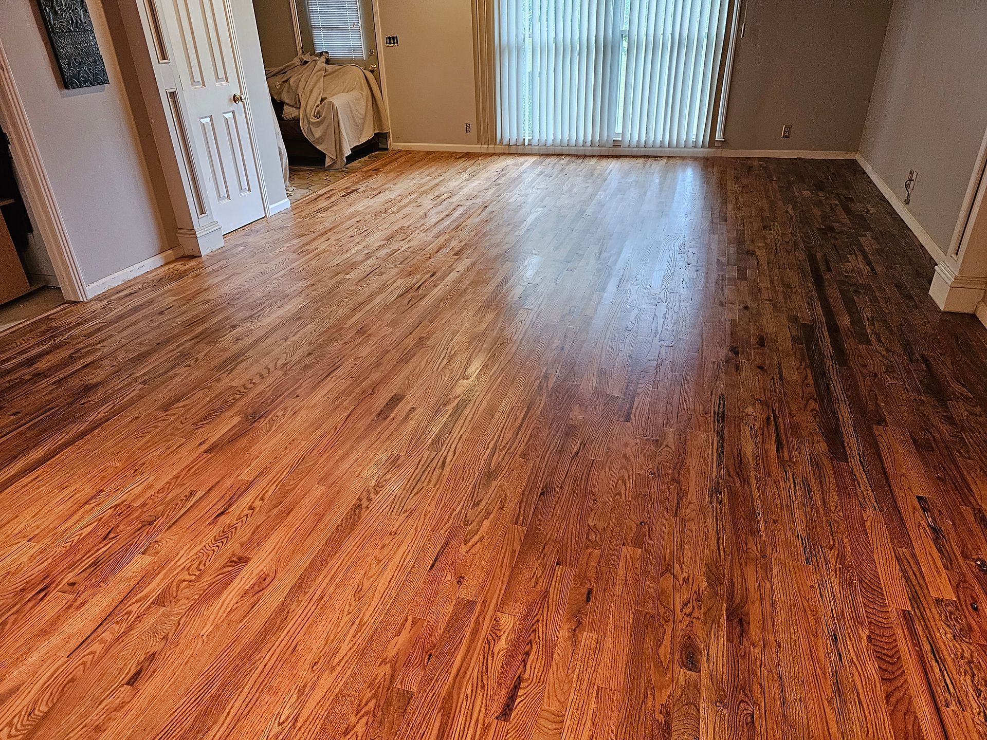 Empty room with hardwood floors and vertical blinds letting in daylight