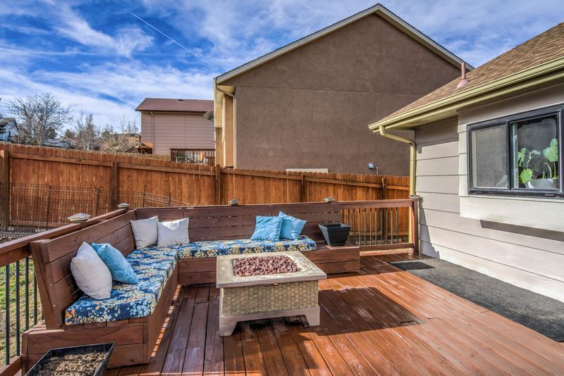 Outdoor wooden deck with built-in bench seating, blue cushions, and a small coffee table, beside a fenced yard.