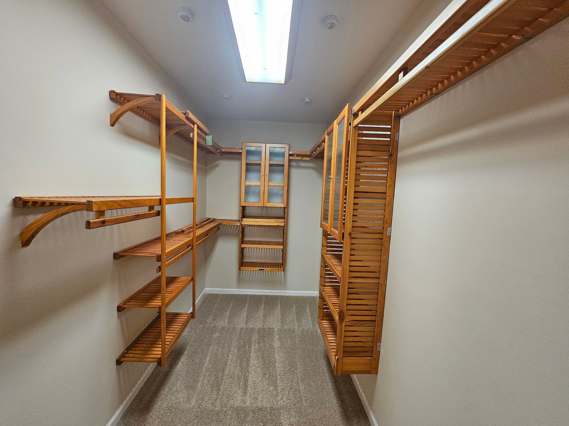 Empty walk-in closet with wooden shelves, hanging rods, and a bright ceiling light
